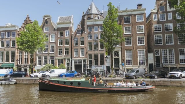 Un bateau-mouche de la compagnie Mokumboot longe les maisons typiques bordant les canaux du centre d'Amsterdam par une journée ensoleillée.